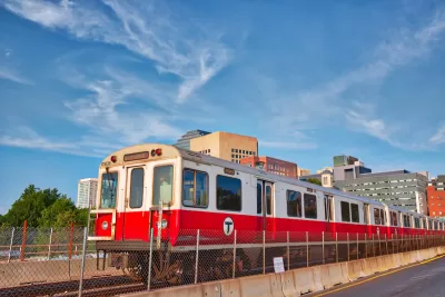 Red T train passing on elevated rail with Boston buildings in background.