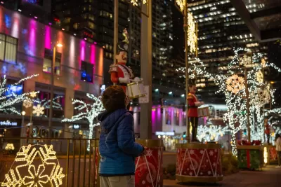 Child looking up at Christmas lights in city at night.