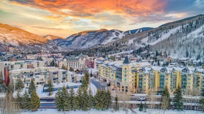 Aerial view of Vail, Colorado in winter with multi-story buildings in foregorund and snowy mountains in background.