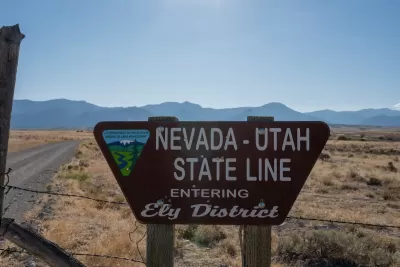 Roadside sign for Nevada Utah State Line "Entering Ely District" with Bureau of Land Management logo with desert mountains in background.