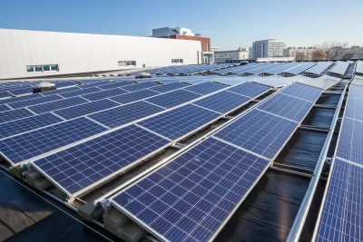 Rows of solar panels on a large rooftop with office or industrial buildings in background.