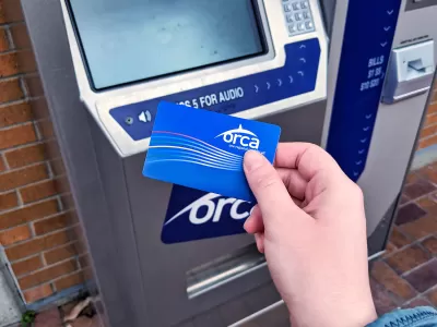 Close-up of person's hand holding blue ORCA transit fare payment card in front of fare payment machine.