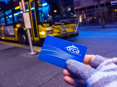 Close-up of gloved hand holding blue Orca transit card with blue and yellow bus in background