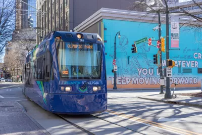 Blue Atlanta Streetcar to Olympic Park on street in downtown Atlanta with colorful mural on building in background.