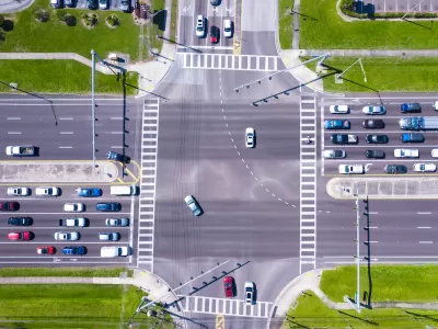 Bird-s eye view of multi-lane road intersection with medians and crosswalks.