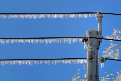 Power lines with dense icicles hanging from them against blue sky.