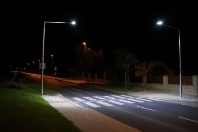 Empty street with crosswalk lit by two tall street lights at night.