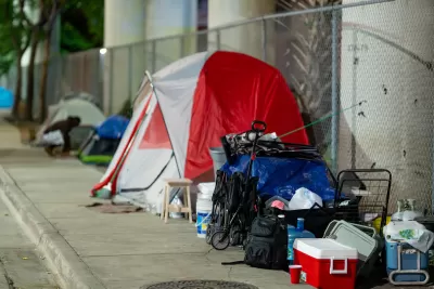 A red and white tent on the sidewalk with other belongings of an unhoused resident in Miami, Florida.