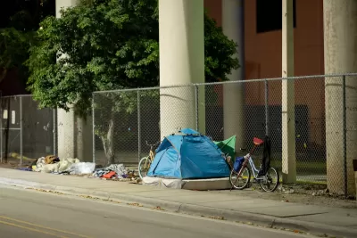 Tent occupied by unhoused resident with bike against fence under underpass in Miami, Florida.