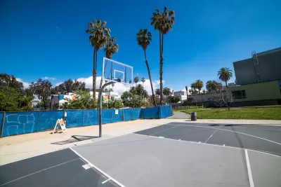 Concrete basketball court with clear glass backboard and palm trees in background in Los Angeles, California.