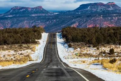 Asphalt road with Bears Ears National Monument rock formations in background.