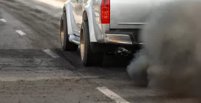 Close-up of driver's side of silver truck with cloud of dirty emissions from tailpipe.