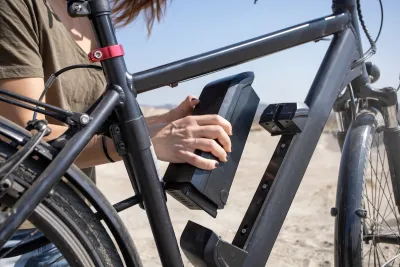 Close-up of person changing battery on black electric bike outdoors.