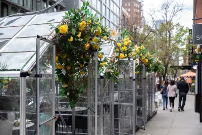 Transparent glass outdoor dining pods with yellow flowers on a sidewalk in New York City during the Covid-19 pandemic.