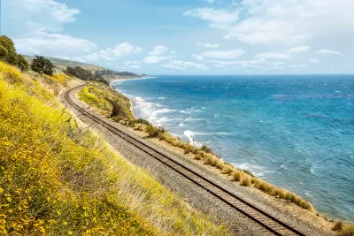 Train tracks along California coast with yellow wildflowers blooming on one side and blue Pacific Ocean on the other.