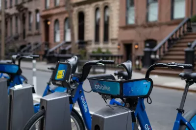 Blue Citi Bike bicycles parked at a station in New York City with blurred brick brownstones in background.