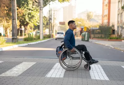 Young man in wheelchair crossing zebra crosswalk.