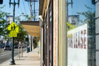Close-up of For Lease sign in window of shop storefront with city sidewalk and vintage street light in background.