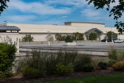 Large blank mall building with only two cars in large parking lot.