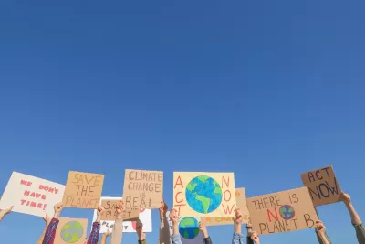 Hands holding up climate change protest signs against blue sky.