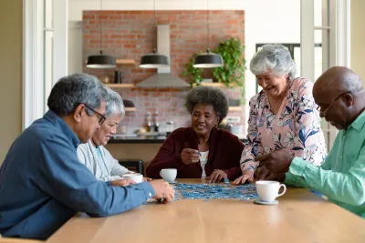 Group of older people sitting at table indoors laughing.