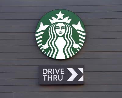 Close-up of Starbucks coffee logo with Drive Thru sign with arrow under it mounted on dark grey wall.