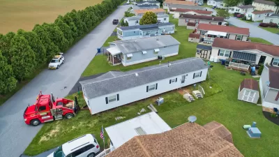 Aerial view of mobile home being moved in a mobile home park by a red truck.