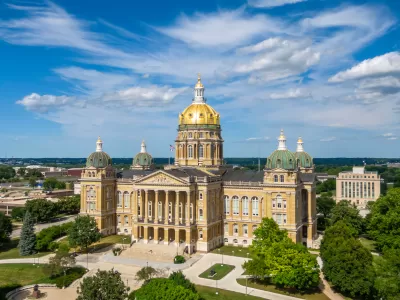 Ornate, tan stone capitol building with a gold dome roof and low-rise city buildings in the background.