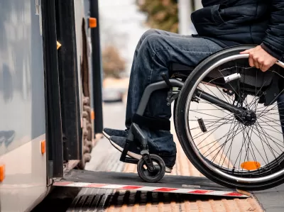 Close-up of person in wheelchair wearing jeans entering public bus on ramp.