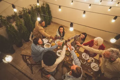 Diverse group of people sitting around a table doing a toast on a patio with warm bistro lights.