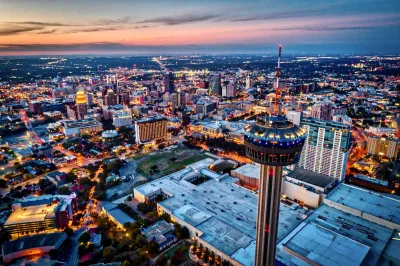 Aerial view of downtown San Antonio, Texas at night with rotating Tower of the Americas in foreground.