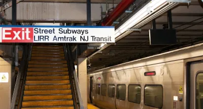 "Street Subway - LIRR - Amtrak - NJ Transit" with Exit sign in front of stairway on subway platform at Penn Station with silver train stopped at right.