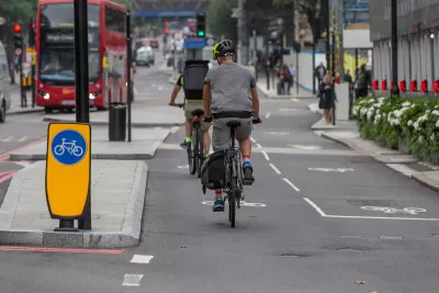 Protected two-way cycletrack on street in London, UK with red double-decker bus in background.
