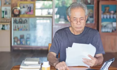 Gray-haired Asian man wearing glasses sitting at wooden table reading documents