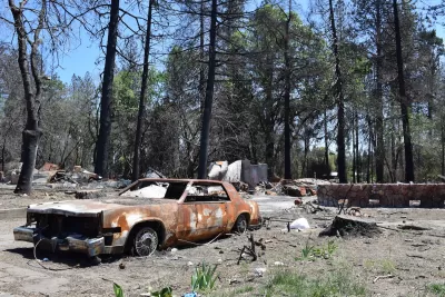 Burned car sits in front of burned house in forest in Paradise, California after the Camp Fire.