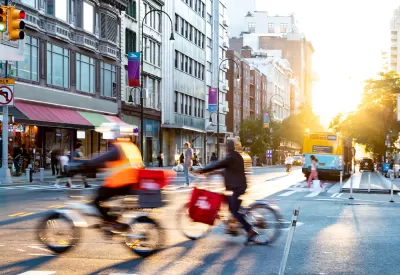 Two delivery bikes riding through intersection in New York City.