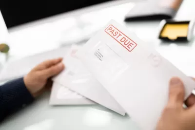 Close-up of hand holding white envelope with red "Past Due" stamp.