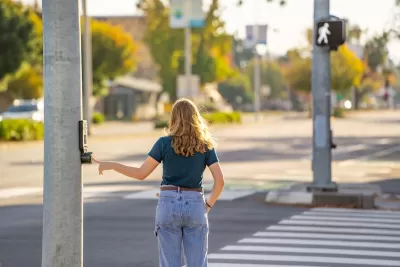 Woman pressing beg button at crosswalk about to cross street.