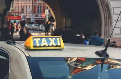 Close-up on yellow and black TAXI sign on top of beige car in central Munich, Germany.
