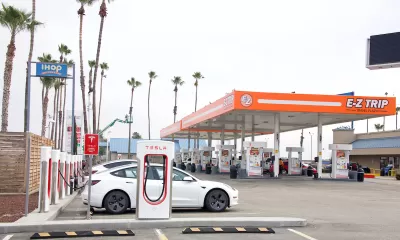 E-Z Trip gas station in Bakersfield, California with orange awning over regular gas pumps and Tesla superchargers with white Teslas charging in foreground.