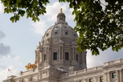 View of Minnesota state capitol dome from side with leafy tree branches slightly obscuring view.
