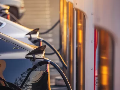 Close-up of row of electric cars plugged into chargers at outdoor station.