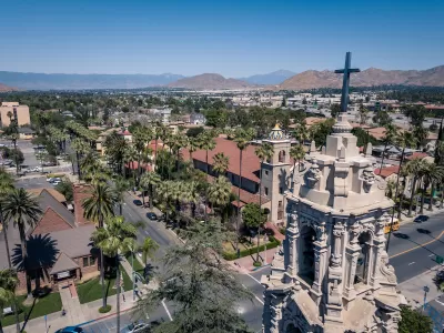 Aerial view of Riverside, California with ornate Catholic church tower in foreground and mountains in the distance.
