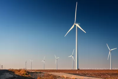 Row of white wind turbines in wide open dirt field in west Texas.