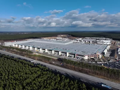 Birds-eye view of a large EV factory and nearby highway, all surrounded by forest.