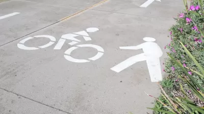 Close-up of white pedestrian and bike symbols painted on concrete path.