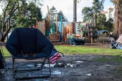 Empty navy blue camping chair with small American flag in front of unhoused encampment in People's Park, Berkeley, California.