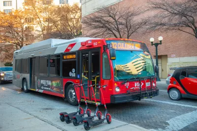 Red public bus on street in San Antonio, Texas with line of four red e-scooters on sidewalk.
