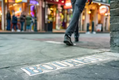 Low close-up of tile BOURBON sign in New Orleans street with pedestrian walking in background.