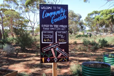 Chalkboard sign at front of a community garden with hours and information.